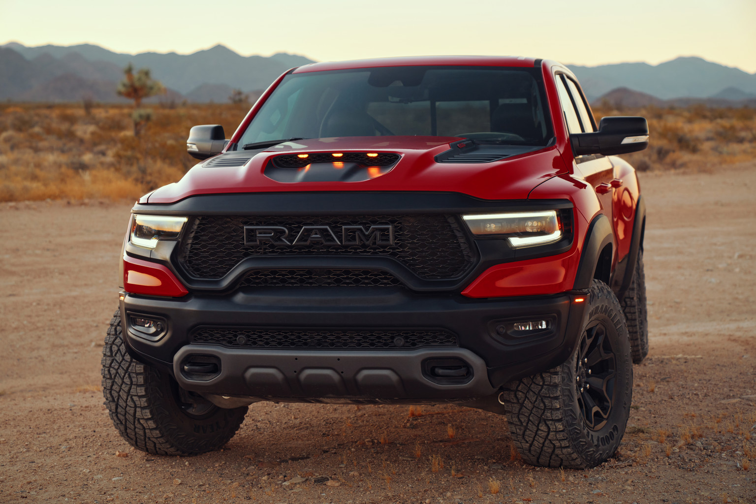A red 2022 Ram 1500 TRX being driven through deep sand in a desert.