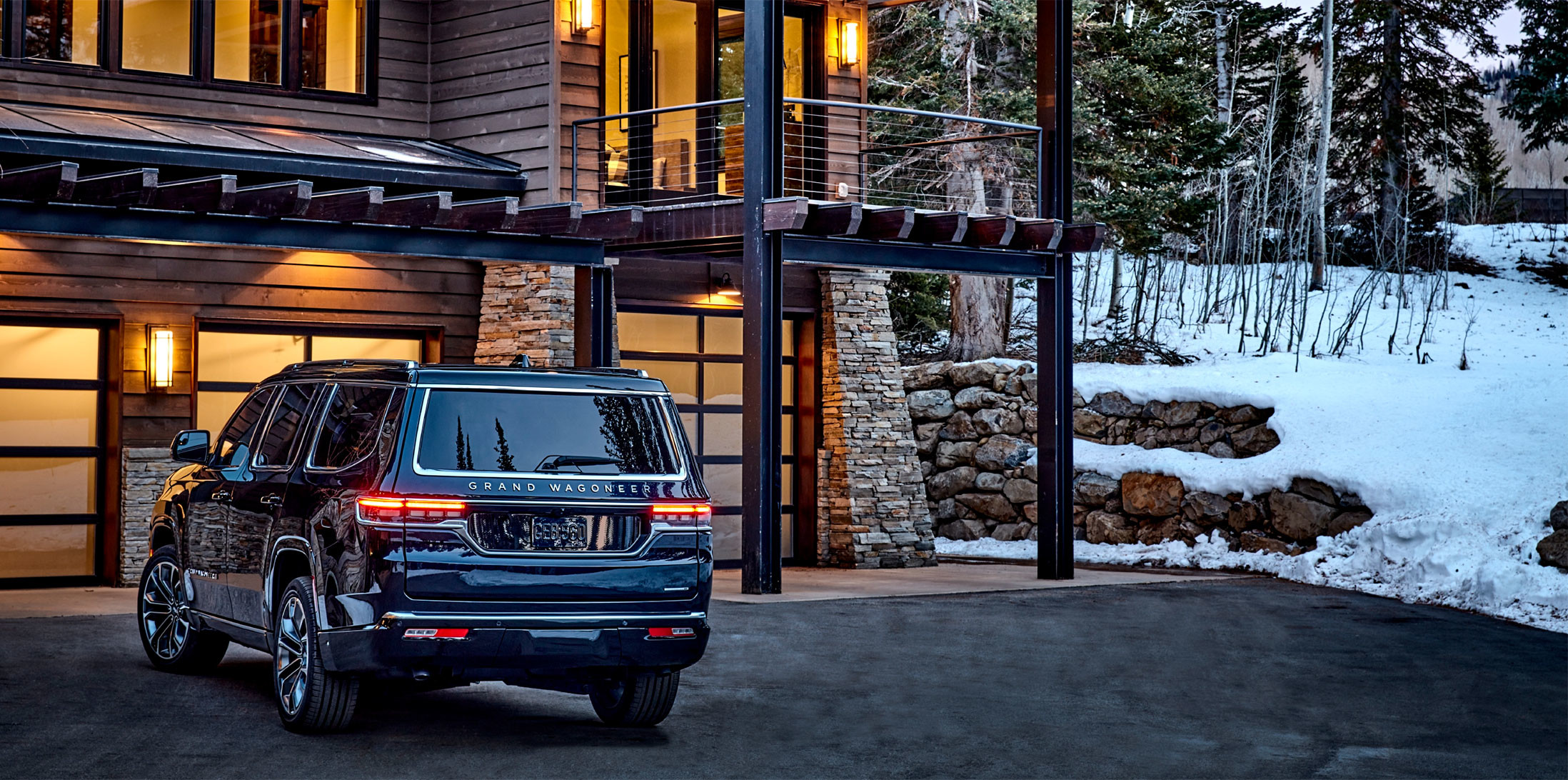 Back view of a black 2023 Grand Wagoneer parked facing a log cabin with trees behind.
