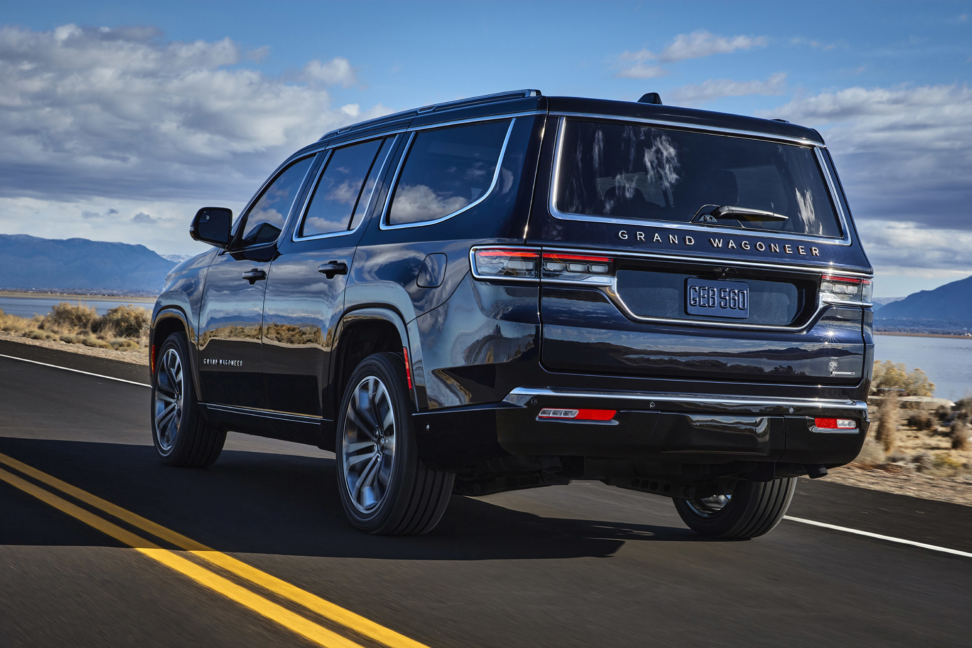 Back view of a black 2022 Wagoneer driving on a road with mountains in the background